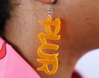 May include: A pair of yellow acrylic earrings shaped like the word "Boss" in a graffiti style font.