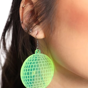 May include: A pair of green disco ball earrings. The earrings are made of clear plastic and have a shiny, reflective finish.