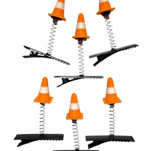 May include: A collection of novelty paper clips featuring miniature orange and white traffic cones attached to black metal clips via springs. The cones have a reflective white band. The clips are arranged against a white background.