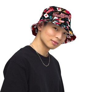 May include: A black bucket hat with a colorful pattern of playing cards, mushrooms, and flowers. The text "Curiouser and Curiouser" is printed on the hat.