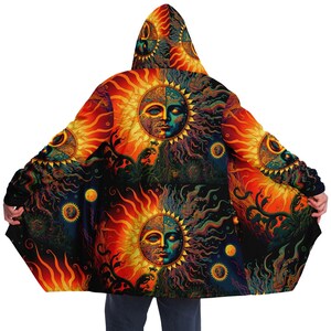 Op de afbeelding: Een capuchon met een psychedelisch zon- en maanpatroon. De cape is zwart met oranje, gele, groene en blauwe details. De zon en de maan hebben gezichten en zijn omringd door sterren.