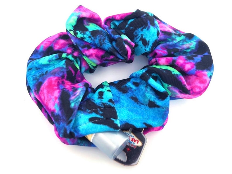 Northern Lights Stashie scrunchie featuring a vibrant mix of blue, teal, pink, and black inspired by the aurora borealis. Made from soft, stretchy fabric with a hidden hook-and-loop fastener pocket for discreet storage of small essentials like cash and keys. Perfect for festivals, raves, and everyday wear.