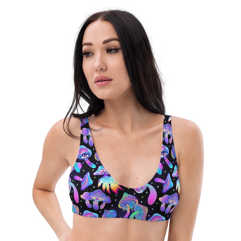 May include: A black bikini top with a vibrant, psychedelic mushroom pattern. The design features colorful mushrooms, stars, and an eye motif in shades of blue, purple, and green. The top has a scoop neckline and wide straps.