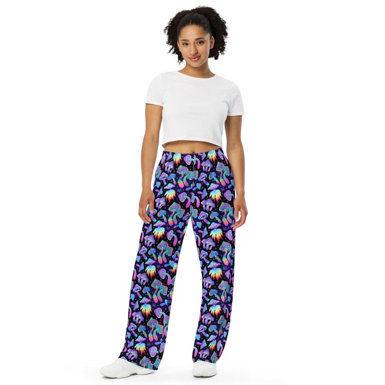 May include: A person wearing a white crop top and black trousers with a colourful mushroom print.