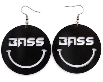May include: A pair of black circular earrings with a white smiley face and the word "BASS" cut out. The earrings have silver hooks.