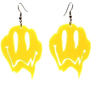 May include: A pair of yellow dripping smiley face earrings. The earrings are made of acrylic and have a silver hook.