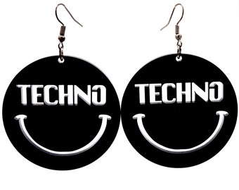May include: A pair of black circular earrings with a white smiley face and the word "TECHNO" written across the face.