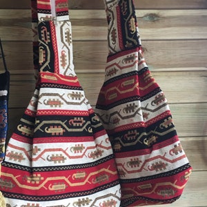 Peut inclure: Deux sacs fourre-tout à motifs rouge, blanc et noir avec des fermetures éclair accrochés à un mur en bois.