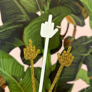 以下が含まれることがあります： 中指の装飾的な置物3つ。1つは白で、他の2つは金色のキラキラです。