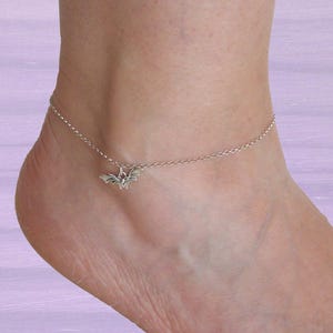 Op de afbeelding: Een delicaat zilverkleurig enkelbandje met een kleine, gedetailleerde vleermuisbedel die aan een fijne ketting hangt. De metalen bedel heeft de vorm van een vleermuis met gespreide vleugels, gecentreerd op de dunne, gepolijste schakelketting.