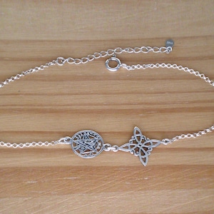 May include: A silver-colored bracelet featuring two charms: a circular pentagram and a four-pointed knot. The bracelet is made of delicate chain links and is set against a wooden background. The bracelet is adjustable.