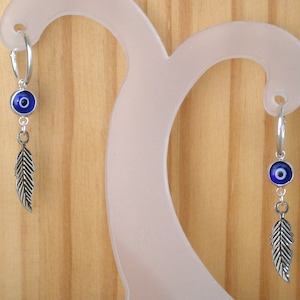 May include: Silver hoop earrings with a blue evil eye charm and a silver feather dangle.
