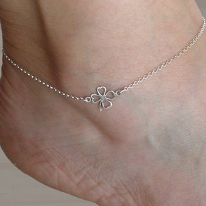 Puede incluir: Un brazalete de tobillo de plata con un dije de trébol de cuatro hojas.
