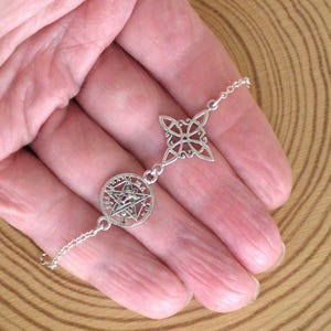 Könnte beinhalten: Ein silbernes Armband mit einem Pentagramm-Anhänger und einem Kleeblatt-Design. Das Armband wird auf einer Hand mit einem Holzuntergrund gezeigt. Das Armband besteht aus einer filigranen Kette.