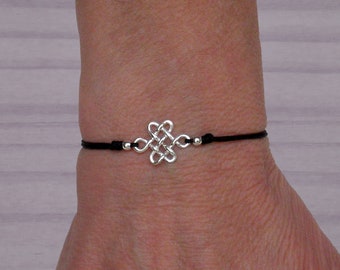 May include: A black cord bracelet with a silver knot charm. The knot is a symbol of eternity and good luck.
