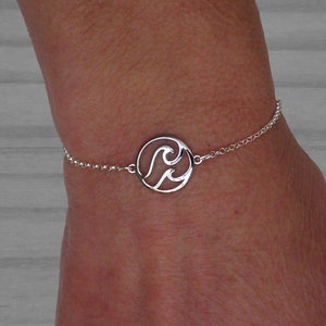 May include: A silver bracelet with a circular charm featuring a cut-out design of two waves.