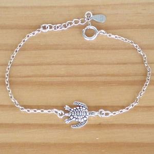 Könnte beinhalten: Ein silbernes Kettenarmband mit einem silbernen Schildkrötenanhänger. Das Armband hat einen Karabinerverschluss.