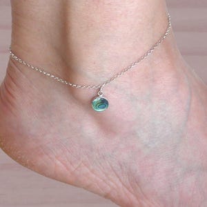 Può includere: Un braccialetto per caviglia in argento con un ciondolo rotondo in madreperla di abalone. La conchiglia presenta colori verdi, blu e iridescenti.