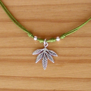 Puede incluir: Un collar de cordón verde con cuentas plateadas y un colgante de hoja plateada.