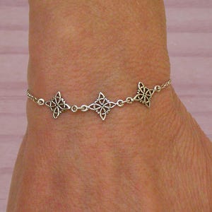Könnte beinhalten: Ein silbernes Armband mit drei verzierten sternförmigen Anhängern, die durch filigrane Kettenglieder verbunden sind. Das Armband wird an einem Handgelenk getragen und zeigt sein aufwendiges Design und den metallischen Glanz. Es ist ein Schmuckstück.