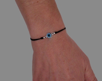 May include: A black string bracelet with a silver charm featuring a blue evil eye.