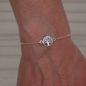 Puede incluir: Un brazalete de cadena de plata con un colgante circular que presenta un diseño de árbol de la vida.