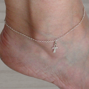 May include: A silver anklet with a small ankh charm. The anklet is made of a delicate chain and the ankh is a simple design.