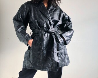 May include: A black leather belted jacket with a long, loose fit. The jacket has a wide collar and a tie belt.