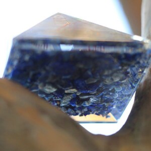May include: A clear glass pyramid filled with blue and gold glitter. The pyramid is resting on a piece of wood.