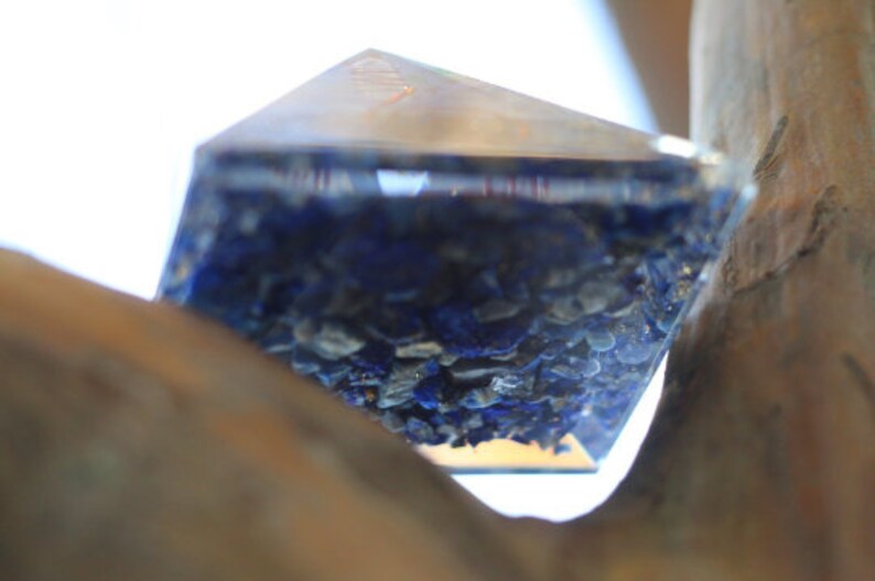 May include: A clear glass pyramid filled with blue and gold glitter. The pyramid is resting on a piece of wood.