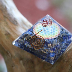 May include: A blue crystal pyramid with a copper wire spiral and a flower of life design. The pyramid is made of lapis lazuli and is sitting on a wooden surface.
