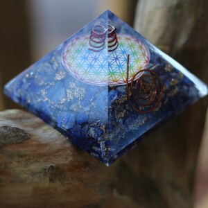 May include: A blue crystal pyramid with a copper wire spiral and a flower of life design inside. The pyramid is made of lapis lazuli and is sitting on a wooden surface.