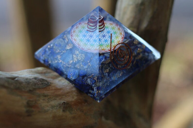 May include: A blue crystal pyramid with a copper wire spiral and a flower of life design inside. The pyramid is made of lapis lazuli and is sitting on a wooden surface.