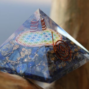 May include: A clear crystal pyramid with a blue and silver base. The pyramid contains a copper wire spiral and a colorful flower of life design.