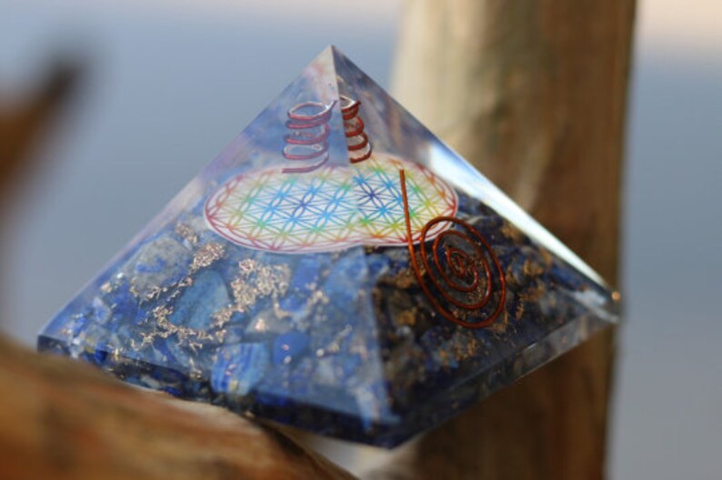 May include: A clear crystal pyramid with a blue and silver base. The pyramid contains a copper wire spiral and a colorful flower of life design.