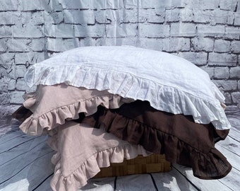Puede incluir: Tres fundas de almohada con bordes con volantes, apiladas una encima de la otra. La funda de almohada superior es blanca, la del medio es marrón claro y la inferior es rosa claro.