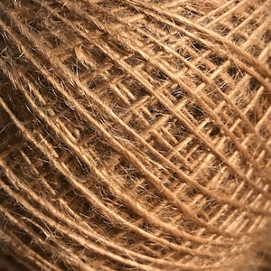 May include: Close-up of a ball of natural brown twine. The twine is tightly wound, creating a textured surface with visible strands and a slightly fuzzy appearance. Ideal for crafting and various DIY projects.