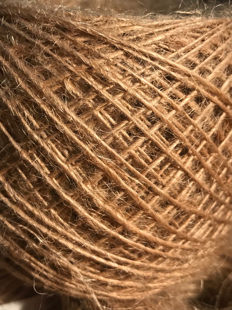 May include: Close-up of a ball of natural brown twine. The twine is tightly wound, creating a textured surface with visible strands and a slightly fuzzy appearance. Ideal for crafting and various DIY projects.