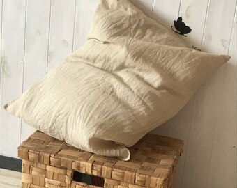 May include: A beige linen pillow resting on top of a woven wicker storage box.