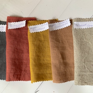 Puede incluir: Cinco muestras de tela en diferentes colores y texturas. Las muestras están etiquetadas con su color y tipo de tejido. Los colores son grafito, terracota, mostaza claro, canela claro y natural.