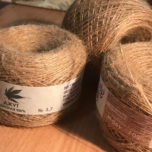 May include: Three spools of natural-colored jute twine are displayed. One spool has a label with a cannabis leaf and the text "ДЖУТ КОНОПЛЯ 100%" and "No 3,7". The other spools have labels with text in a foreign language.