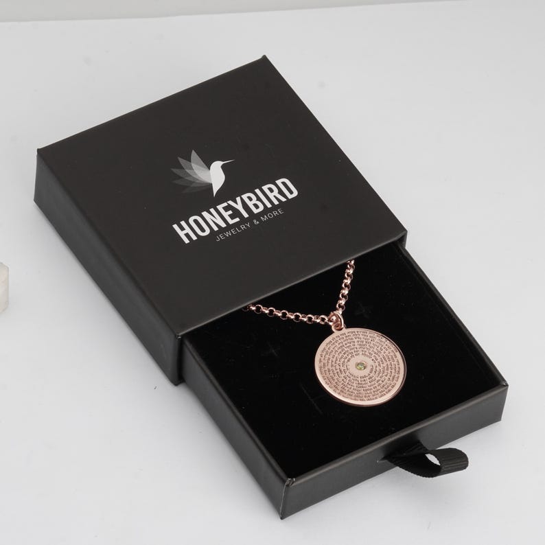 May include: A rose gold circular pendant necklace with a central stone and engraved text, presented in a black sliding jewellery box. The box lid features a white hummingbird logo and the text HONEYBIRD JEWELRY & MORE printed in white.