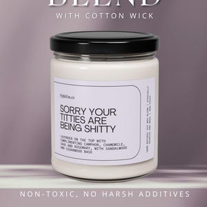 May include: A white soy wax candle in a clear glass jar with a black lid. The label reads: 100% NATURAL SOY WAX BLEND WITH COTTON WICK, SORRY YOUR TITTIES ARE BEING SHITTY, LAVENDER ON THE TOP WITH COMPLIMENTING CAMPHOR, CHAMOMILE, SAGE AND ROSEMARY.