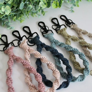 May include: Six colorful braided keychains with black metal key rings. The keychains are made of twisted cotton rope in shades of pink, beige, blue, teal, and green.