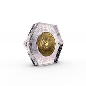 Puede incluir: Una moneda de criptomoneda Ethereum de color dorado con el texto "Ethereum Decentralized Scalable" mostrado en la moneda, se muestra en una vitrina hexagonal de acrílico transparente.