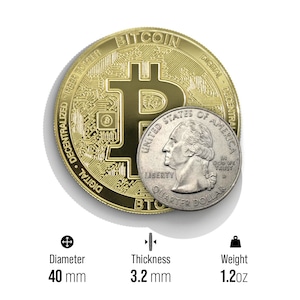 May include: A gold-colored Bitcoin coin with the Bitcoin symbol and the words "Digital Decentralized Peer to Peer" and "Bitcoin" around the edge. The coin is 40 mm in diameter and 3.2 mm thick. It weighs 1.2 ounces. A silver US quarter is shown for size comparison.