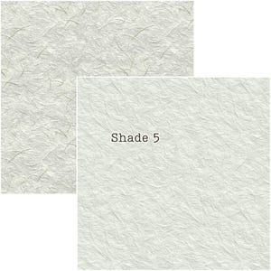 Puede incluir: Dos hojas de papel texturizado blanco roto. Una es rectangular, la otra cuadrada con el texto "Shade 5". El papel tiene un aspecto delicado y fibroso con sutiles variaciones de tono, sugiriendo una calidad artesanal.