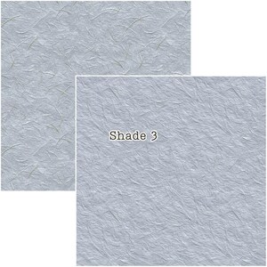 Puede incluir: Dos piezas rectangulares de papel azul claro texturizado con sutiles fibras doradas. La pieza m&aacute;s grande tiene el texto "Shade 3" en blanco, con una fuente sans-serif. El papel tiene un aspecto ligeramente arrugado, lo que sugiere un material hecho a mano o natural.