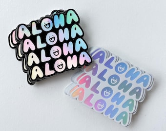 May include: A stack of iridescent rainbow holographic stickers with the word "ALOHA" and a smiley face on each sticker.