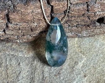 May include: A green moss agate pendant on a silver cord necklace. The pendant is teardrop shaped and has a natural, organic look.